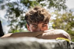 Young man falls his head down on his arms, smiling and looking up