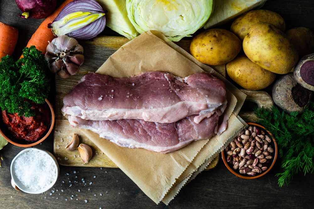 Ingredients for hearty soup with meat surrounding cutting board