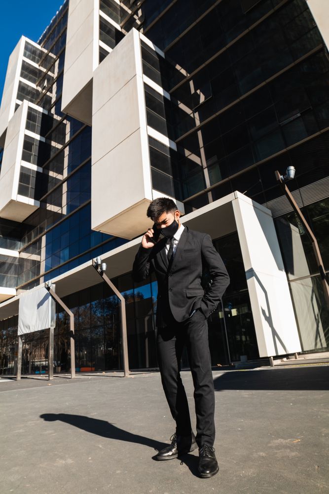 Businessman in mask speaking on smartphone in city