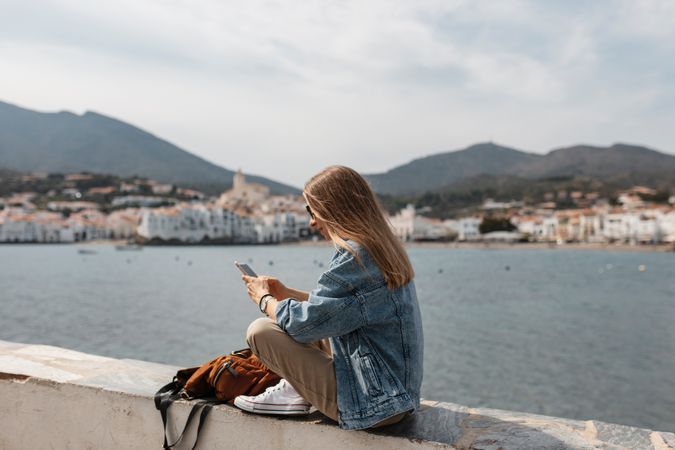 Woman using a smartphone sitting on a ledge