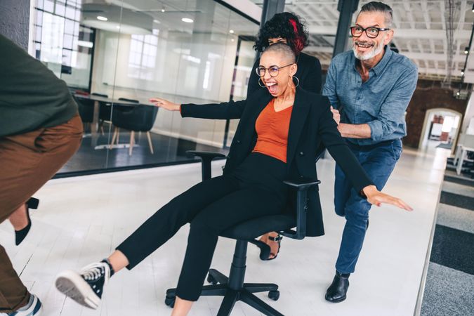 Group of businesspeople having fun during break by pushing each other in office chairs