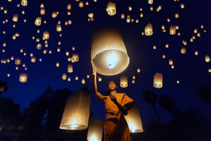 Young monk standing under lit lanterns in the sky