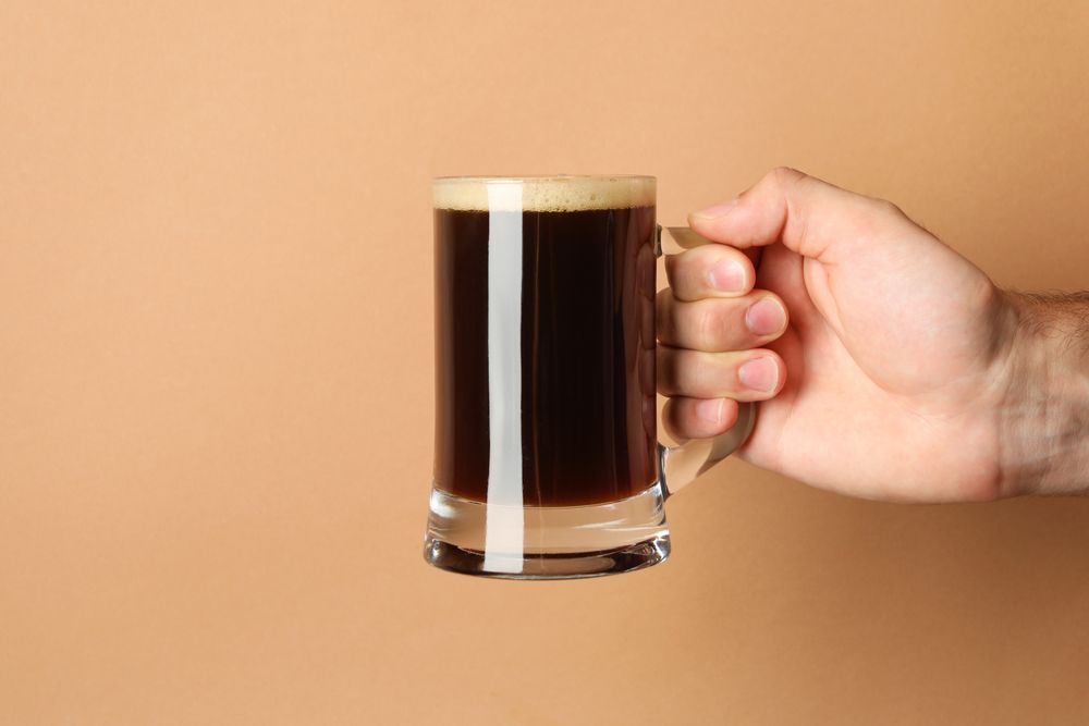 Male hand hold glass of beer on brown background