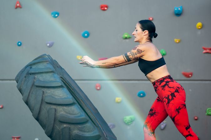 Side view of athletic woman lifting a truck wheel in a gym