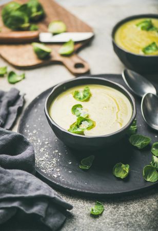 Bowls of Brussels sprout soup, on dark plate, garnished with fresh sprouts, vertical composition