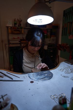Female master processing jewelry with saw in dark workshop