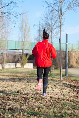 Back of woman in red jogging outdoors in park on sunny fall day