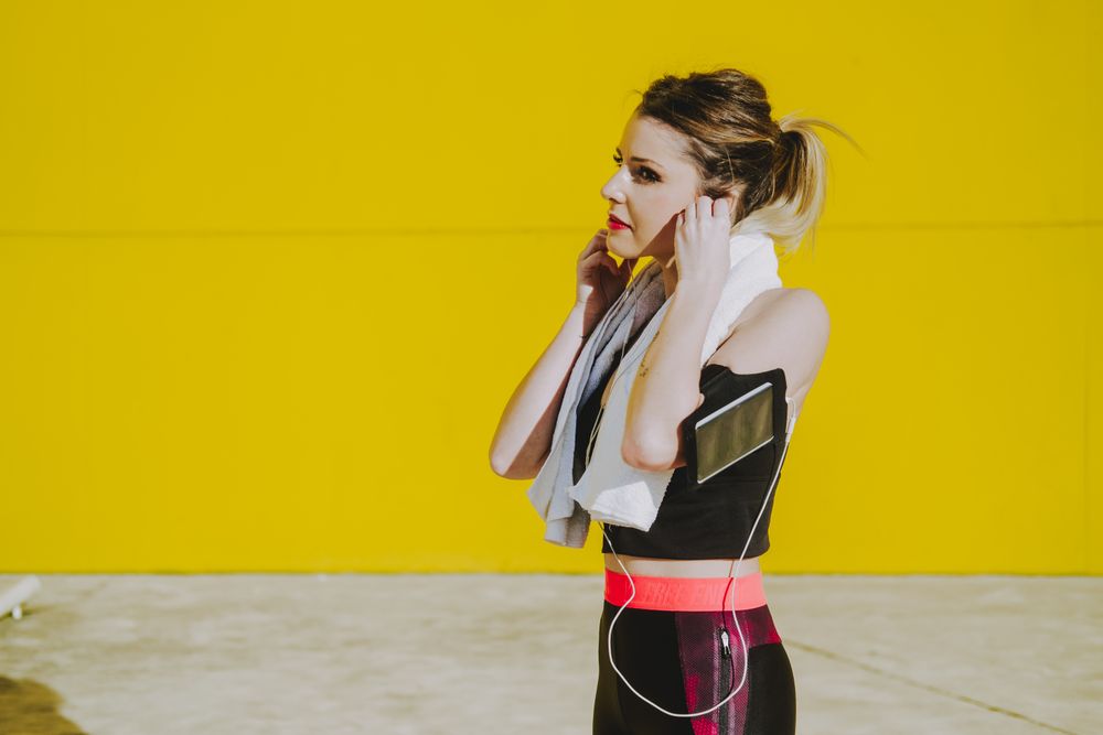 Woman with earphones running near wall