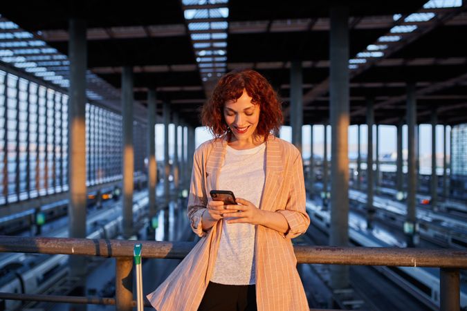 Smiling young woman browsing phone at station