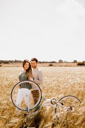 Sincere lovers posing by bicycle on rye field