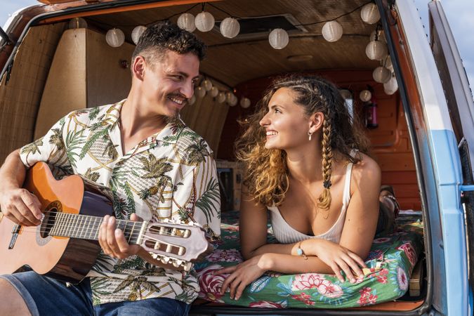 Amorous man plying on guitar and looking at woman in trunk of car