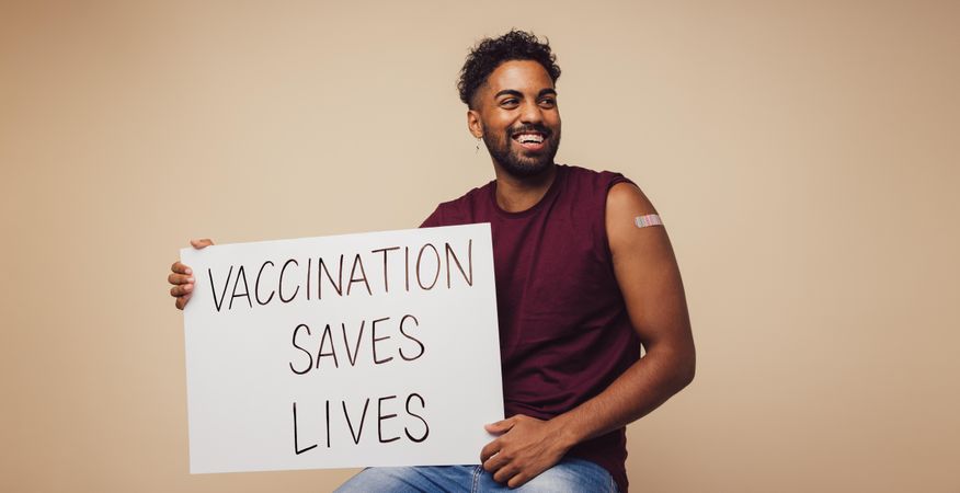 Man holding a poster with "vaccination saves lives" written