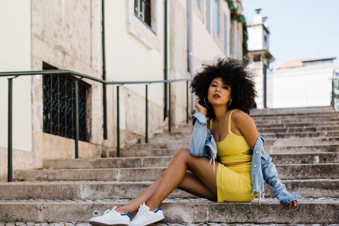 Stylish Black female sitting in stairs with railing outdoors