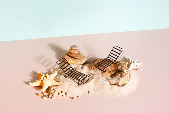 Miniature beach lounge chairs on the sand on pastel background