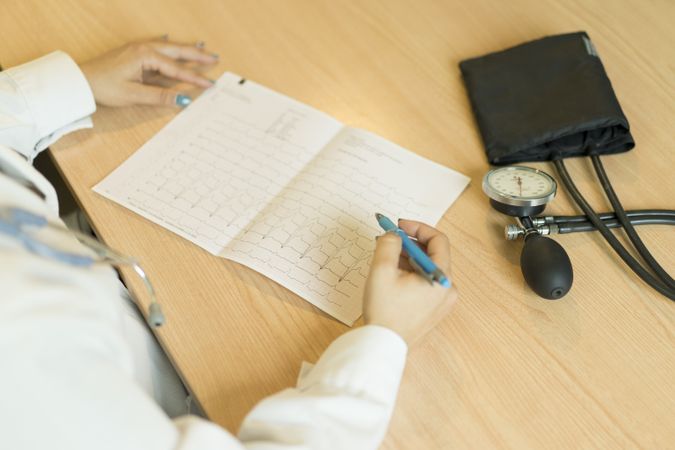 Anonymous young female doctor with document at table near pulsometer