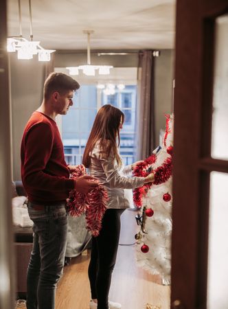Young couple expecting baby arranging Christmas tree at home