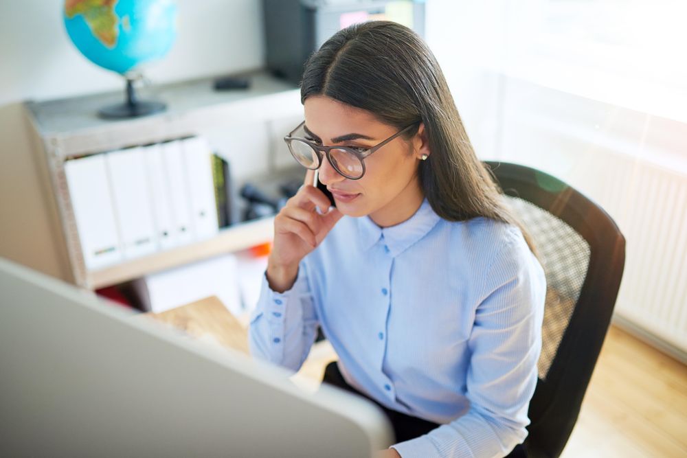 Looking down at woman talking on cell phone while working on her desktop computer