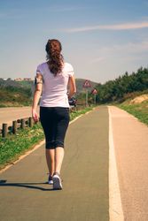 Back of woman in athletic gear strolling along road, vertical