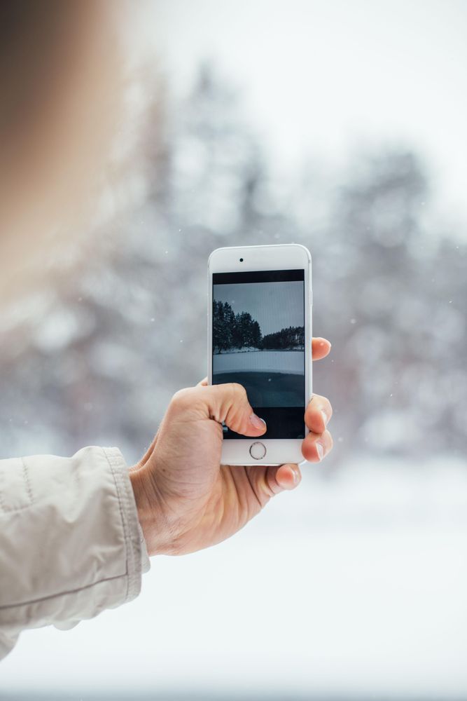 Hand taking photo of wintry scene with phone, vertical