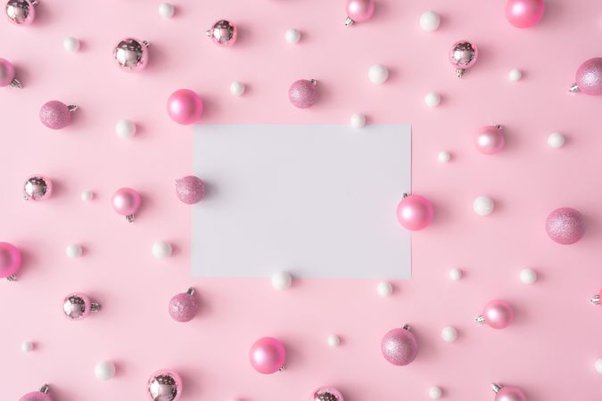 Different shades of pink and light-colored baubles on a pink background with paper card