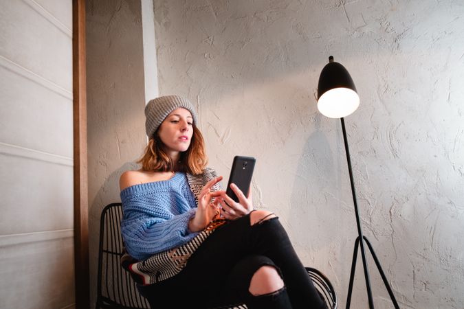Woman in sweater and hat on the mobile phone and sitting near wall