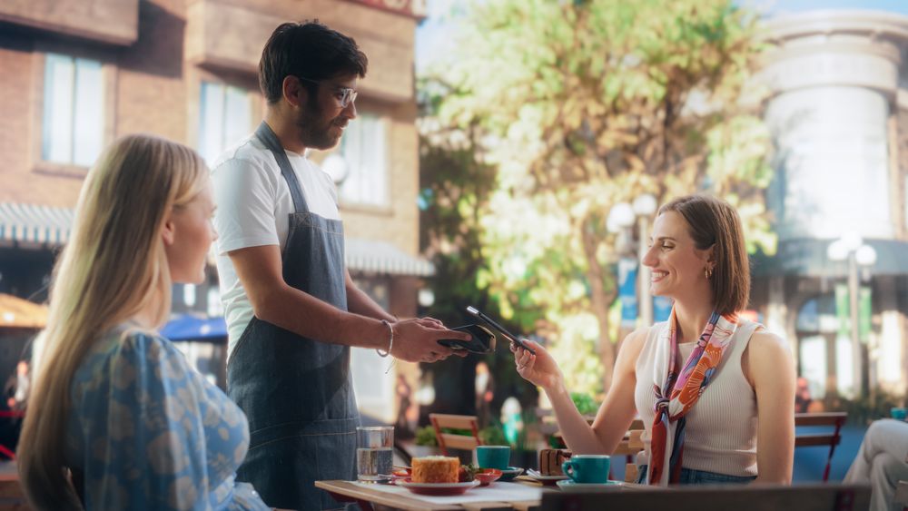 Two Female Friends Ordering Delicious Cake Desserts From a Member of the Staff in a Cafe.