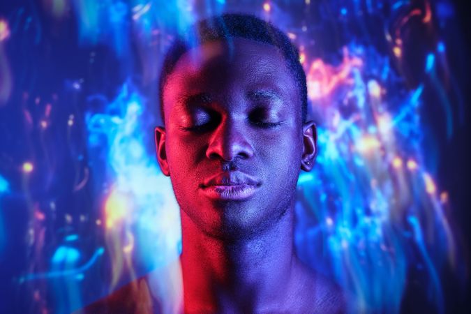 Emotionless Black man with eyes closed standing in blurred light