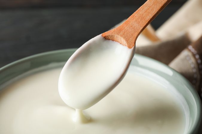 Bowl of sour cream yogurt, spoon and towel on wooden background
