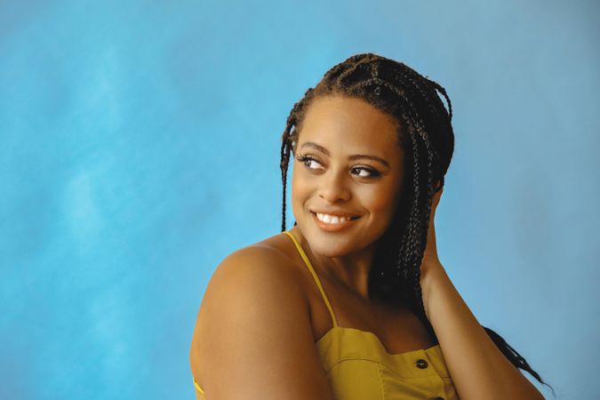 Portrait of smiling female with long braided hair looking away in yellow shirt, copy space