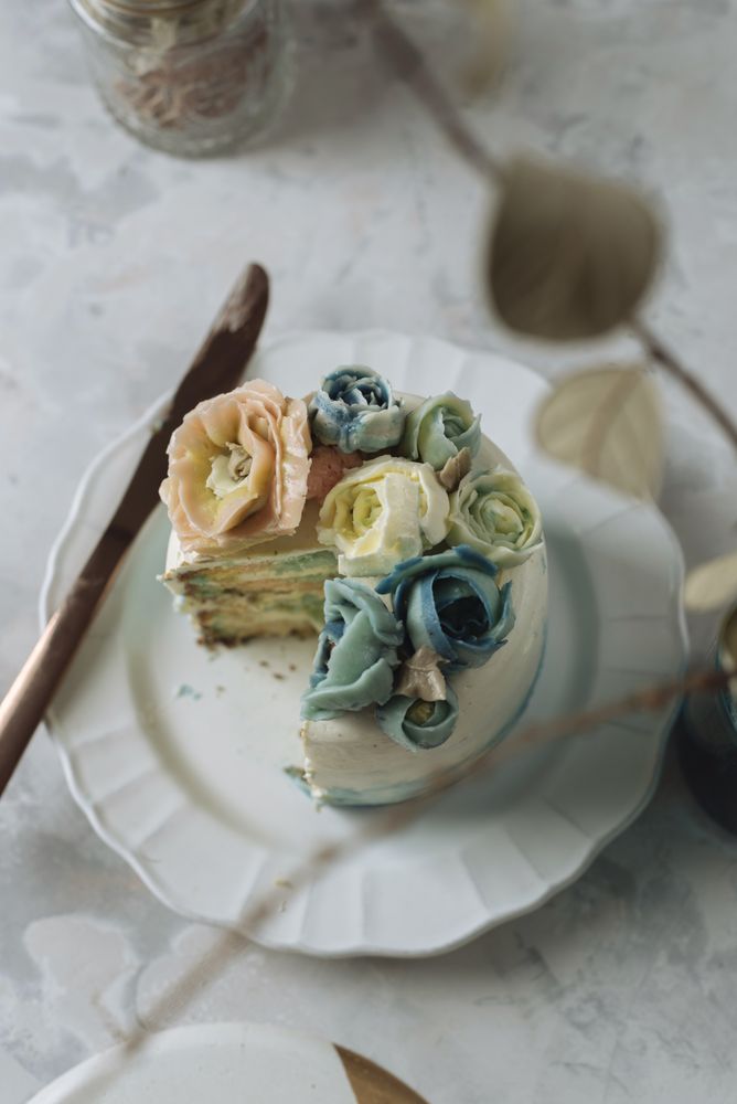 Portion of rainbow cake, filled with chantilly cream, and decorated with buttercream flowers