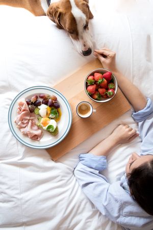 Woman sharing food with dog at bed