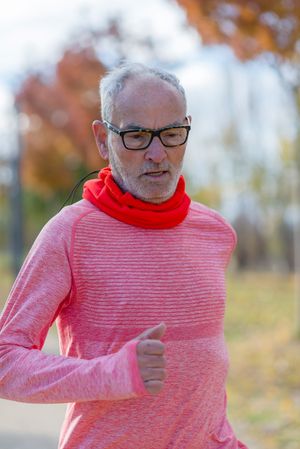 Grey haired man with glasses working out in park in the fall