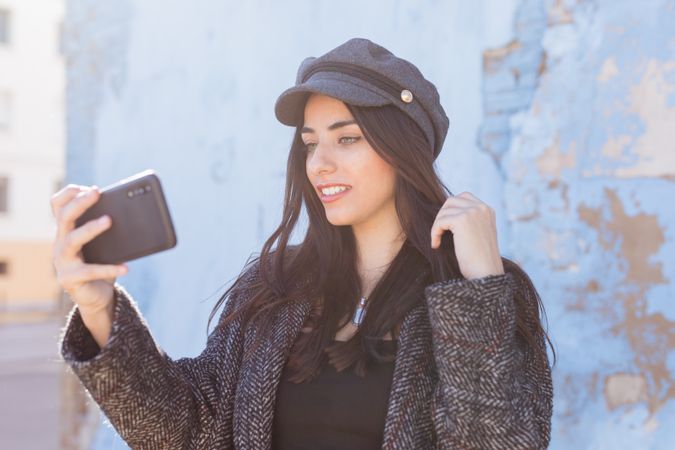 Charming Hispanic lady taking selfie near wall