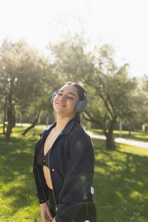 A young woman smiles happy while listening music with headphones, during a walk through the park, Zaragoza, Spain