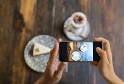 Faceless person taking picture of cake and coffee