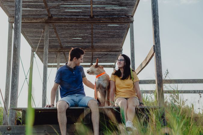 Cheerful adult couple playing with dog at countryside