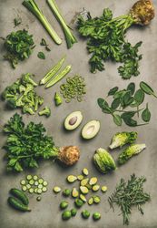Arrangement of fresh green sliced garden vegetables on concrete surface