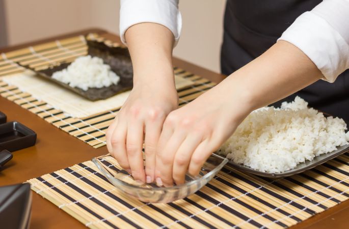 Woman chef wetting fingers to close Japanese sushi rolls with rice on a nori seaweed sheet