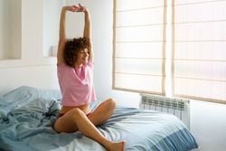 Smiling woman waking up in blue bed and stretching her arms