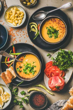 Yellow lentil soup bowls, vegetable garnishes, spices, top view, vertical composition