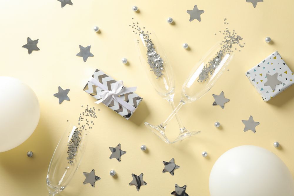 Composition with champagne glasses, gifts and glitter on beige background, top view