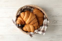 Top view of wicker basket with croissants on wooden table