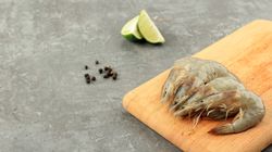 Uncooked prawns on board being prepared before cooking, with slices on lime and peppercorns