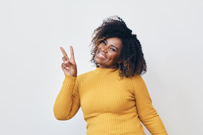 Studio shot of a happy Black woman in yellow shirt making the peace sign