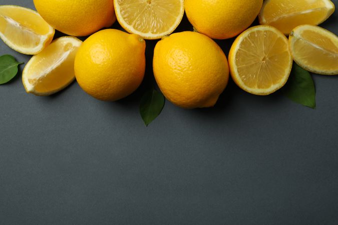Fresh lemons with leaves on dark background, top view. Ripe fruit