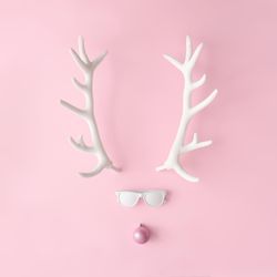 Reindeer face made of sunglasses and pink bauble on pink background