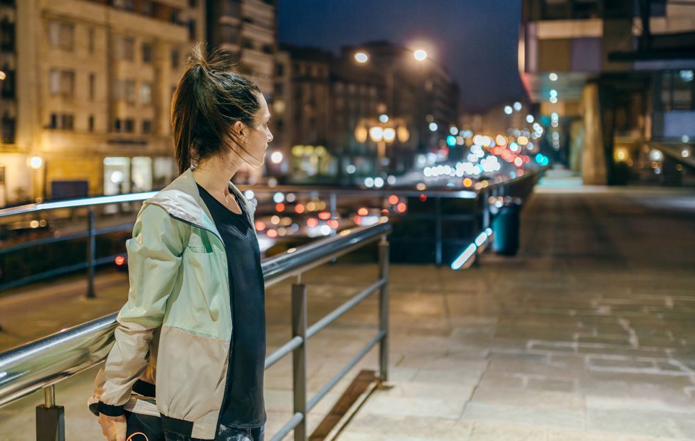 Active woman stretching her legs next to banister before training at night in town