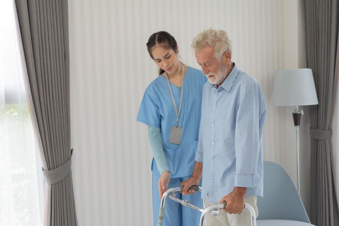 Nurse helping mature male patient with walker
