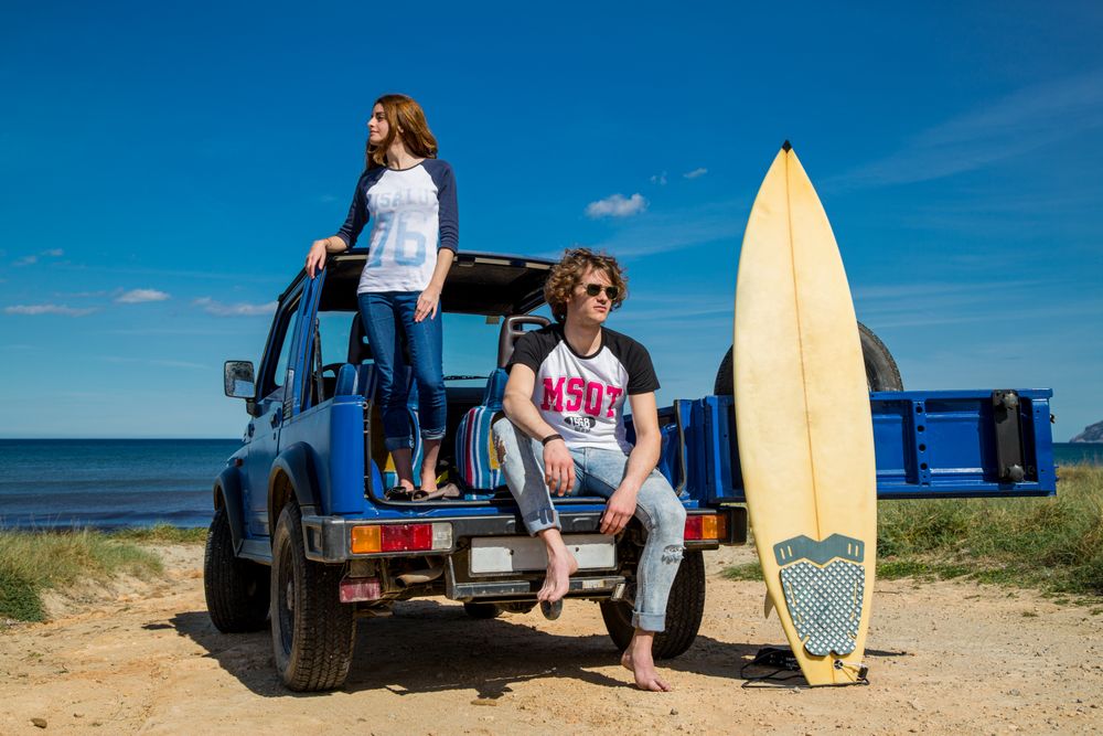 Guy with surfboard and woman standing on car