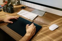 Cropped image of a person drawing on tablet beside computer